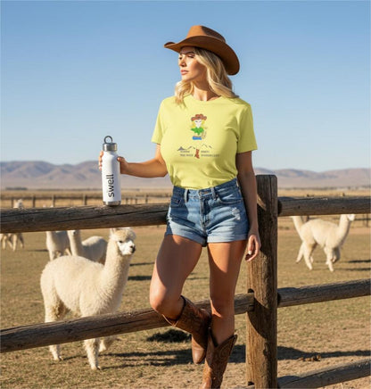 Woman in a yellow t-shirt with a cowgirl graphic and cowboy hat holding a Swell water bottle with alpacas in the background.