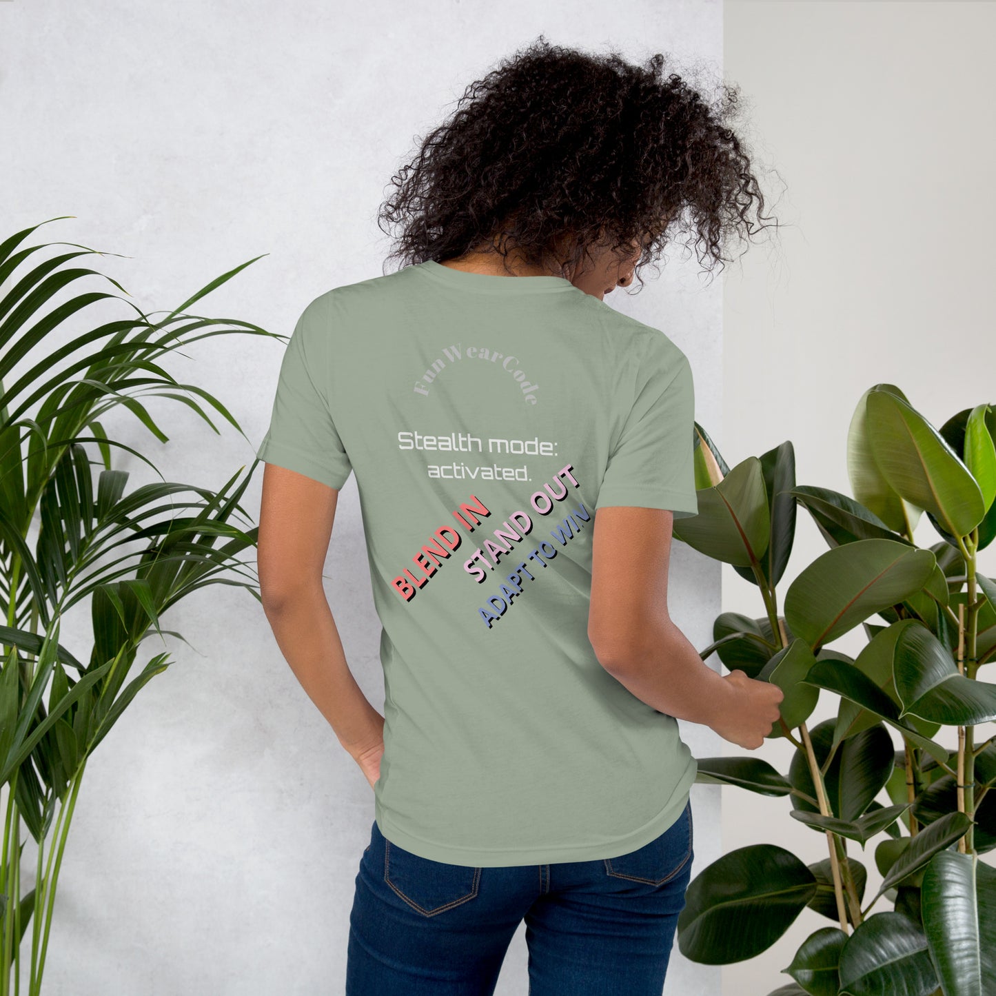 Person wearing a green t-shirt with a 'Fun Wear Code' text logo and colorful texts on the back, standing between two plants.